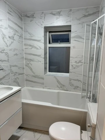 Completed bathroom viewed from the doorway, with marble-effect wall panels, bath, shower screen and vanity