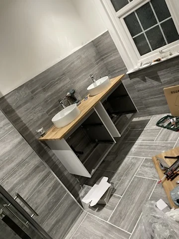 Twin basins and a timber-effect vanity in a grey tiled bathroom nearing completion