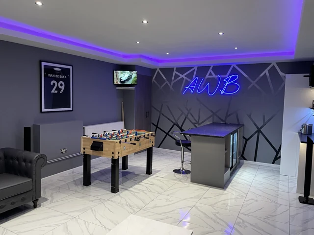 Finished games room with grey seating, table football, a bar and colourful lighting