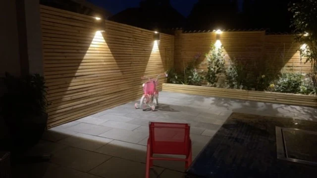 Finished patio with horizontal timber fencing, planted borders and warm garden lighting