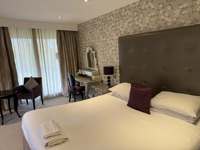 Furnished hotel bedroom with a patterned feature wall, upholstered headboard and layered curtains