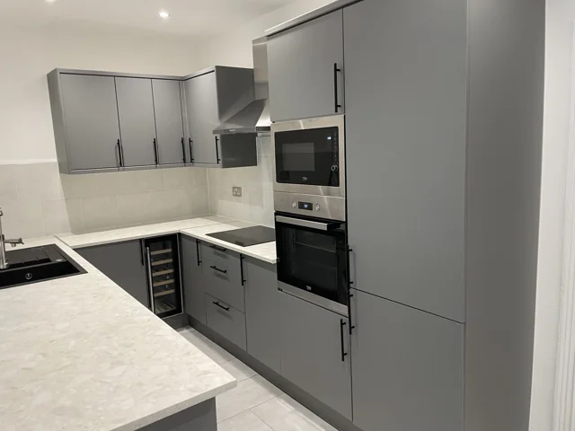 Grey kitchen cabinetry, integrated oven and pale stone-effect worktops