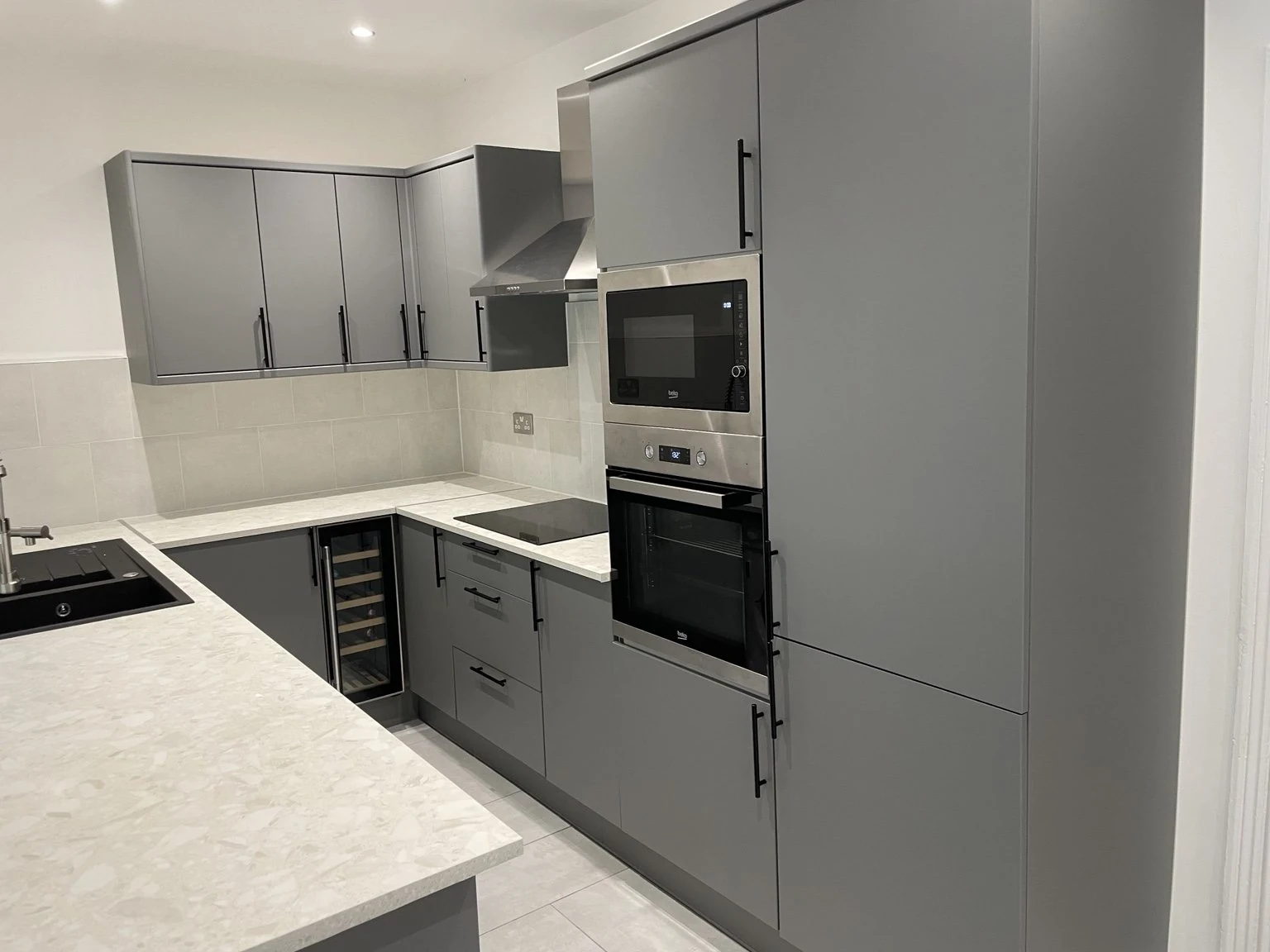 Finished kitchen with grey cabinetry, integrated oven and pale stone-effect worktops