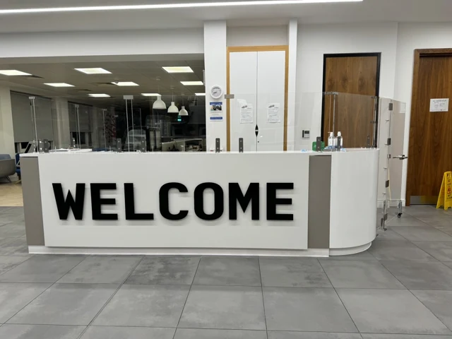 Front view of the installed white reception desk with bold WELCOME lettering and grey inset panels